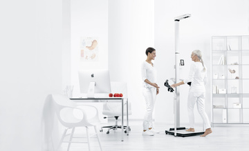 Ein Arzt und ein Patient stehen neben einem Bioimpedanzgerät für eine Messung der Körperzusammensetzung.